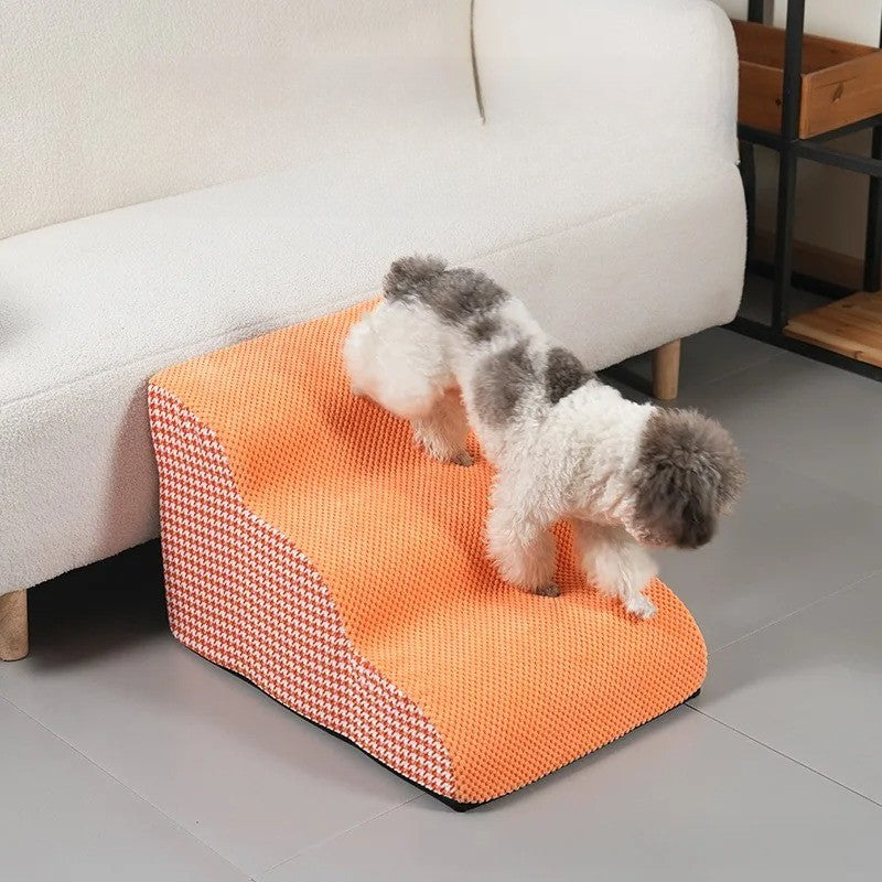Petit chien montant un escalier orange à 3 marches en mousse, stable et antidérapant, parfait pour accéder au canapé en toute sécurité, disponible chez Museau Dort