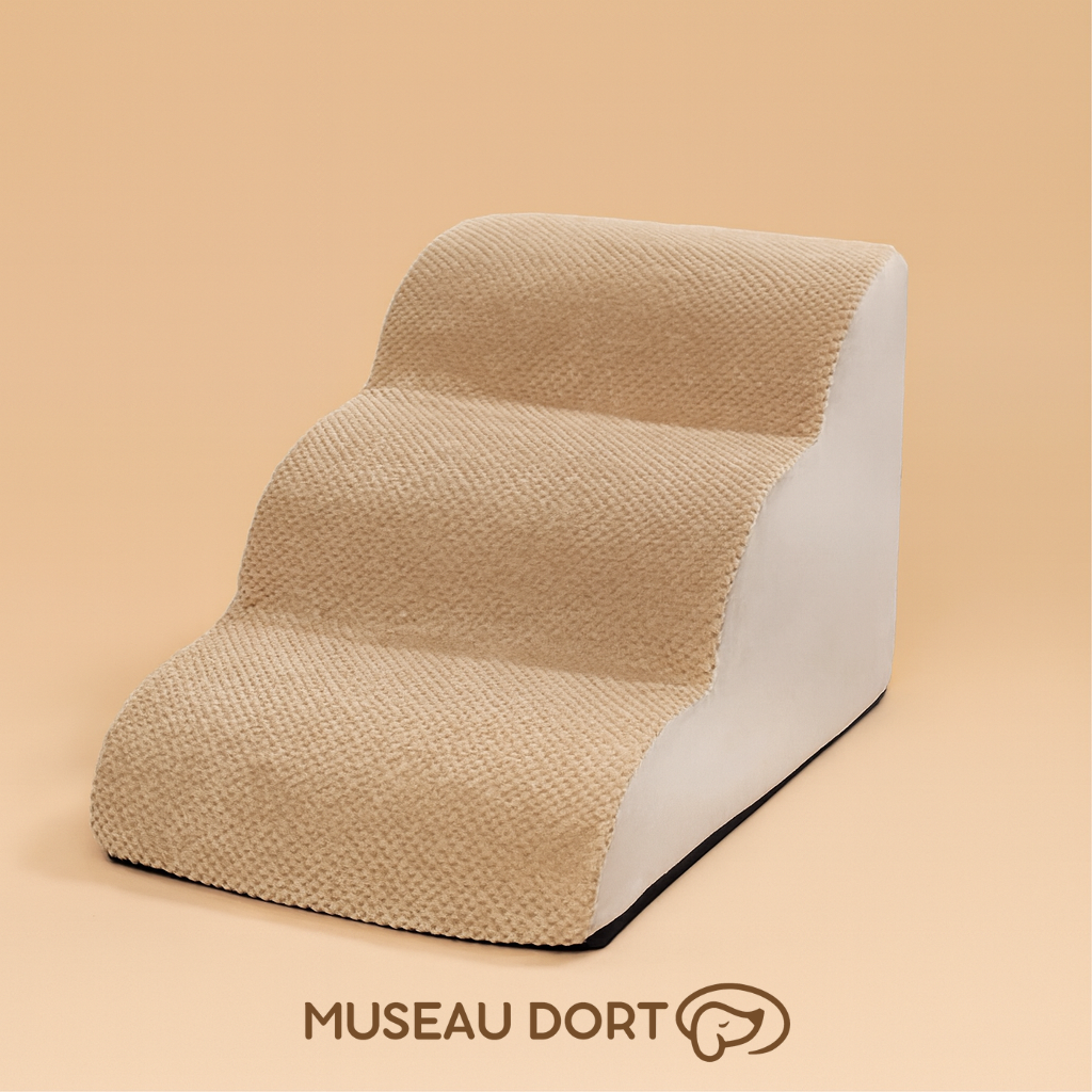 Escalier pour chien trois marches en tissu beige présenté sur fond studio couleur sable, modèle confortable. Disponible chez Museau Dort