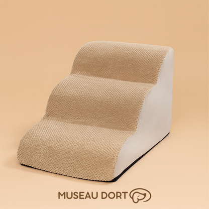 Escalier pour chien trois marches en tissu beige présenté sur fond studio couleur sable, modèle confortable. Disponible chez Museau Dort