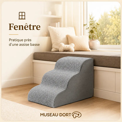 Escalier en mousse pour chien placé près d’une assise basse sous une fenêtre lumineuse.