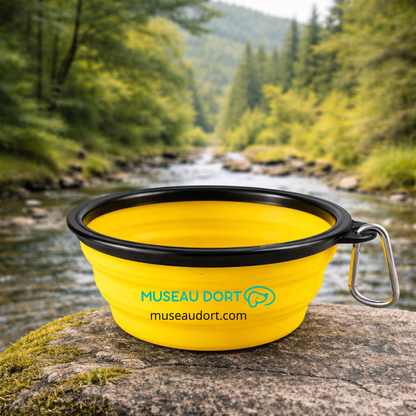 Gamelle pliable pour chien en silicone jaune avec mousqueton, posée en nature près d’une rivière, Museau Dort