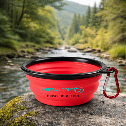 Gamelle pliable pour chien en silicone rouge avec mousqueton, posée en nature près d’une rivière, Museau Dort
