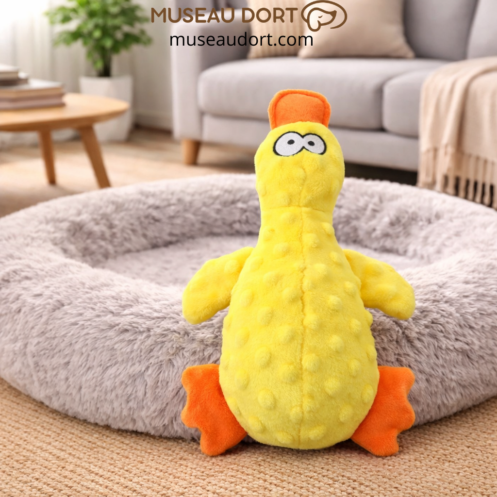 Jouet canard jaune pour chien sur lit gris, stimulant ludique et dentaire. Disponible chez Museau Dort.