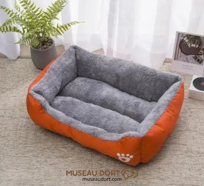 Lit pour chien cocon orange avec rebords gris, couchage confortable installé dans un intérieur lumineux, Museau Dort
