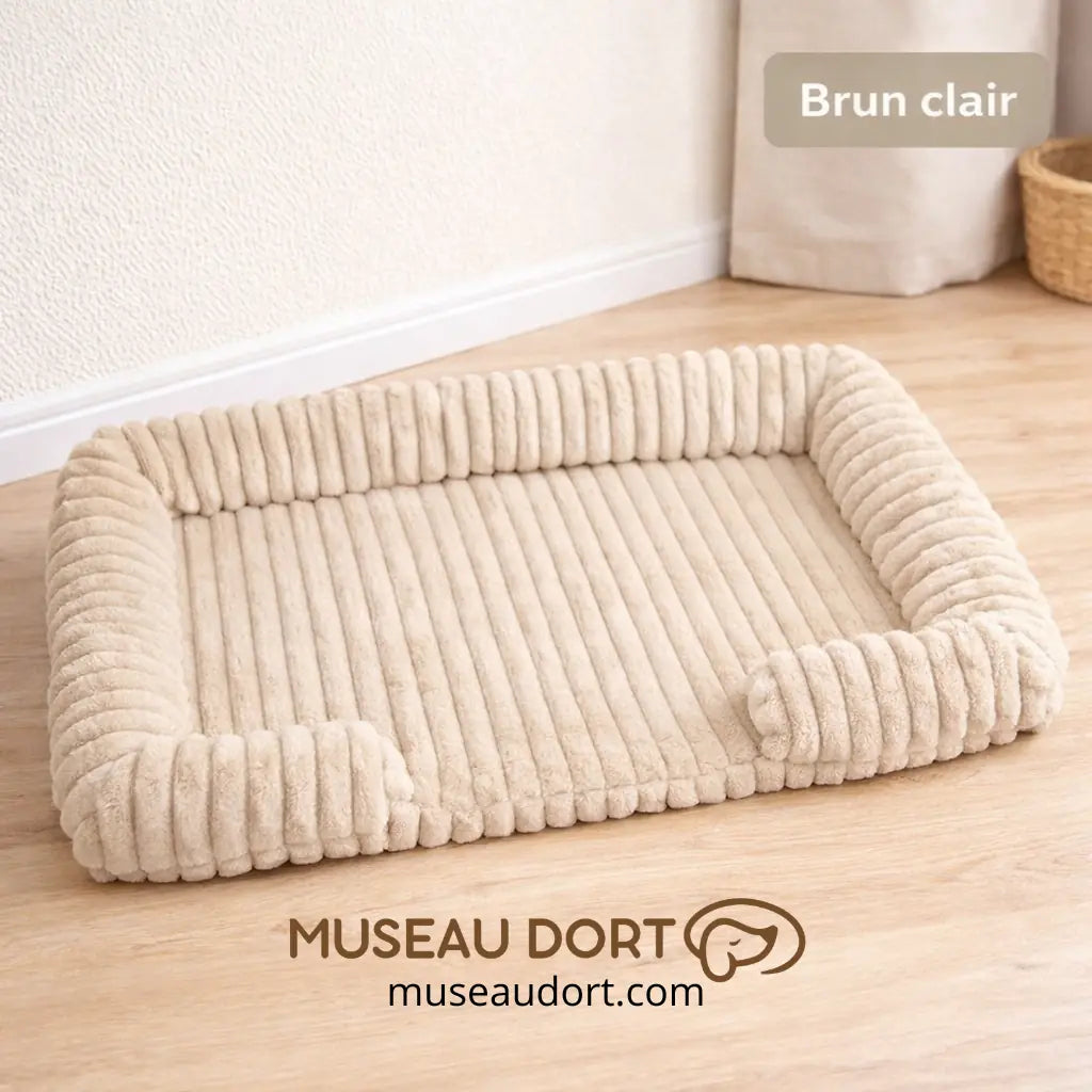 Lit pour chien orthopédique brun clair avec rebords rassurants dans un salon, disponible chez Museau Dort