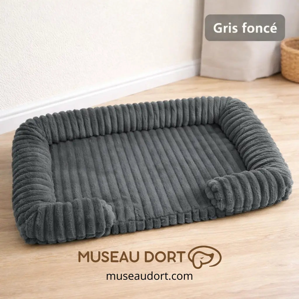 Lit pour chien orthopédique gris foncé avec rebords rassurants dans un salon, disponible chez Museau Dort